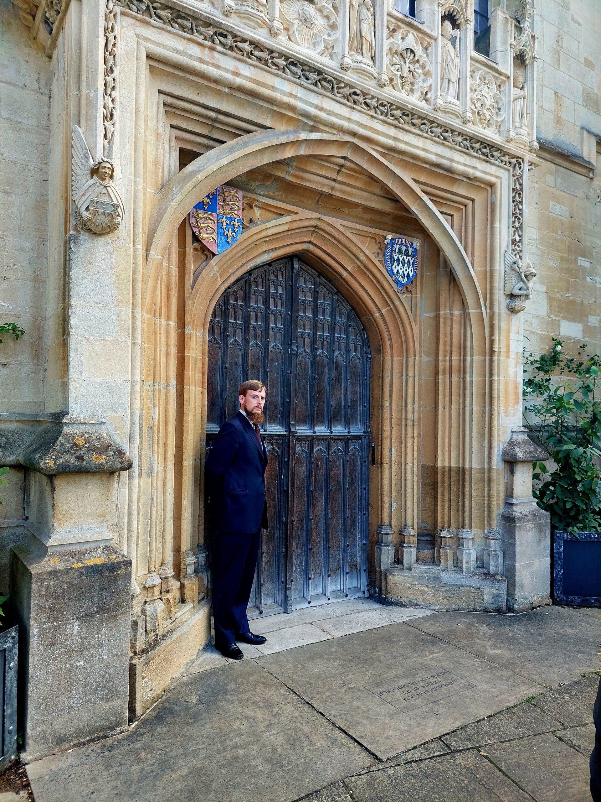 Colour photograph of Edmund Racher, Magdalen College Chapel Administrator, posed outside the Chapel door in St John's Quadrangle, 2025.